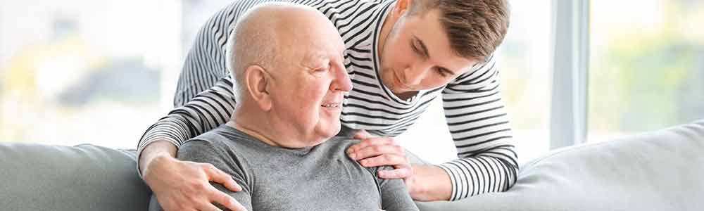A young male caregiver talking with the elderly man he cares for