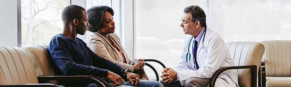 A mother and her caregiver son talking with a doctor at a health care clinic