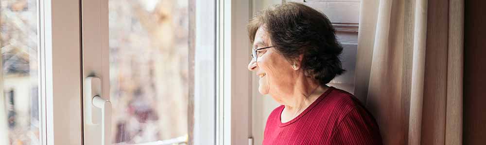 An elderly woman looking out her front door, smiling
